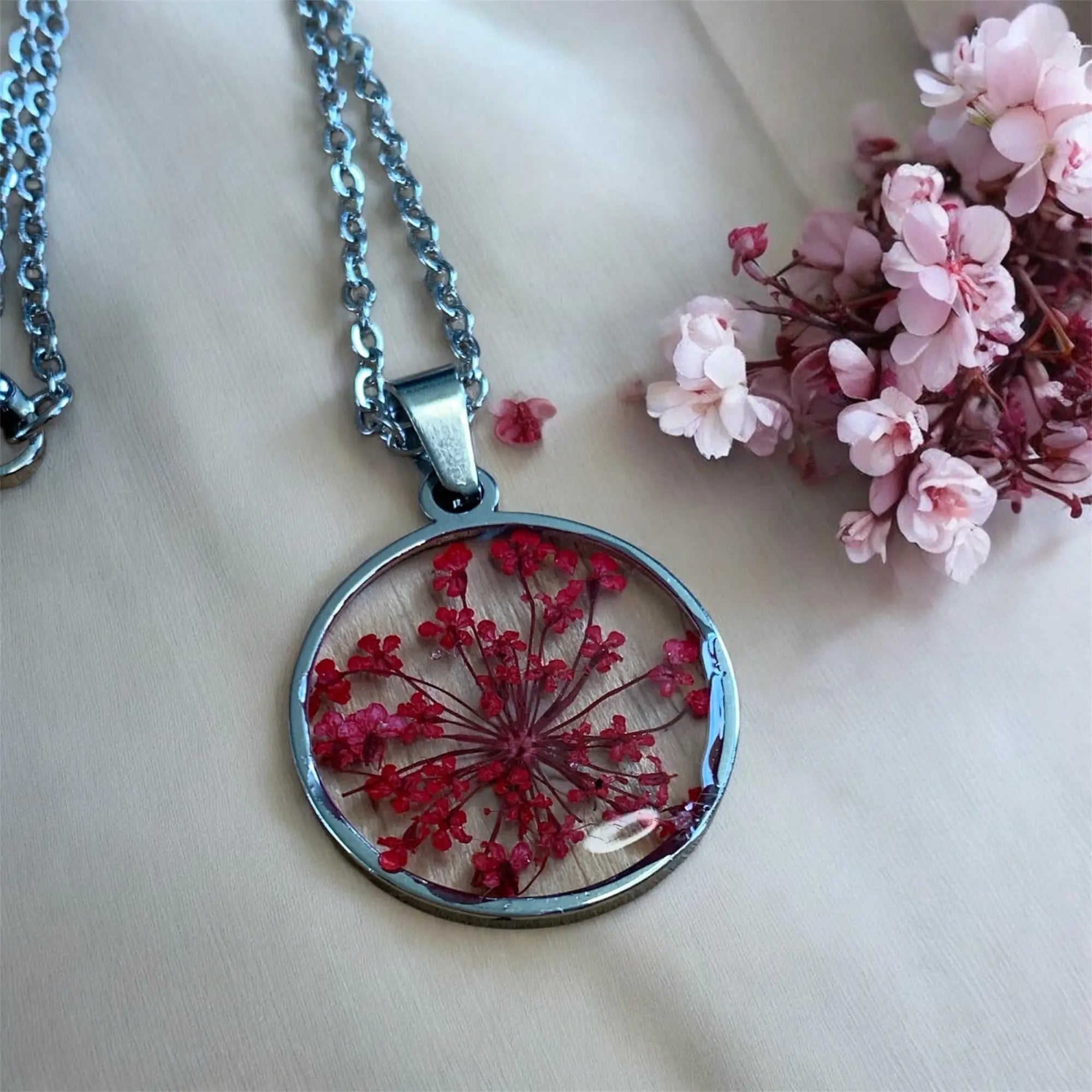 Pendentif circulaire avec cadre et chaîne en métal argenté contenant des fleurs rouges préservées en résine claire collection bijoux