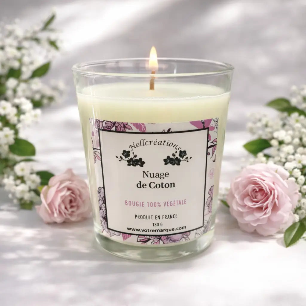 Une bougie en cire de soja crémeuse allumée dans un bocal en verre transparent avec une étiquette fleurie nellcréations gamme ambiance