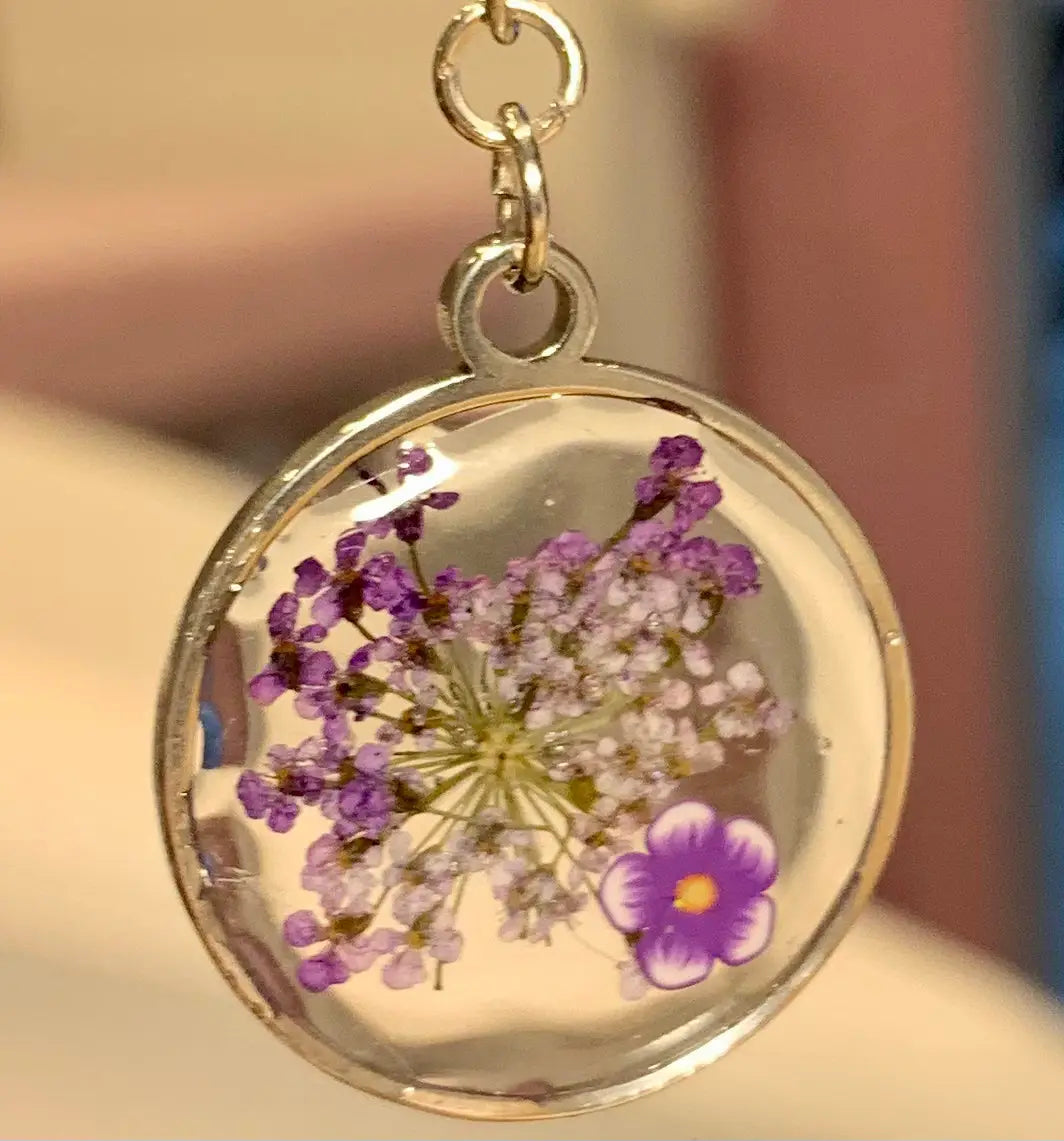 Boucles d’oreilles violettes fimo avec pendentif circulaire en résine claire encadré de métal argenté contenant fleurs sauvages préservées violettes et blanches