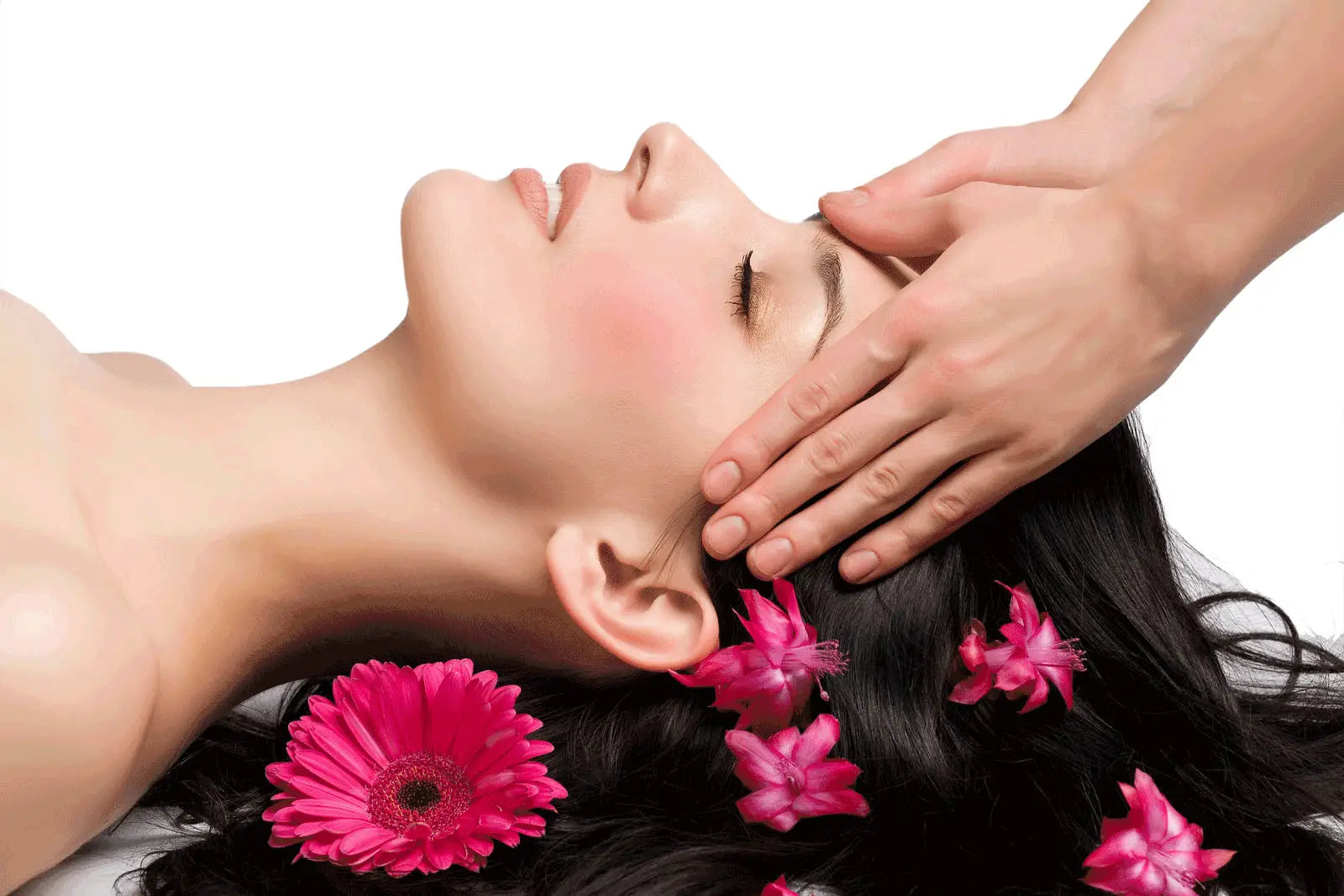 Une femme aux longs cheveux noirs allongée avec des gerberas roses pour un massage crânien et visage de 25 minutes